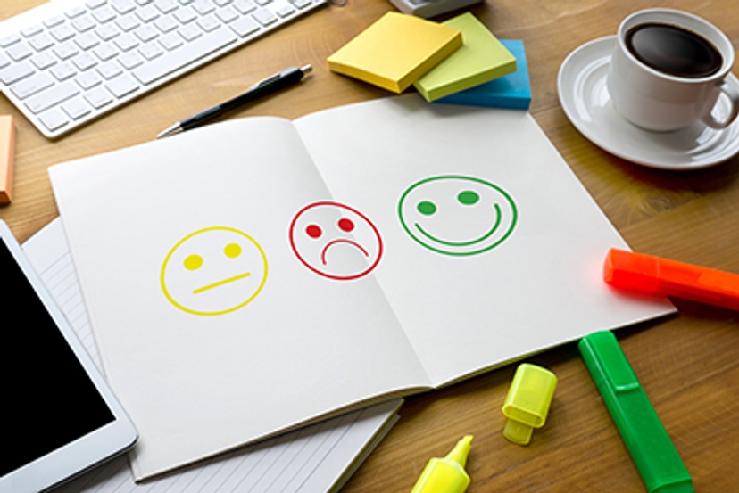 yellow neutral, red unhappy and green smiley face drawings on a white page with highlighter pens, post-its and devices surrounding