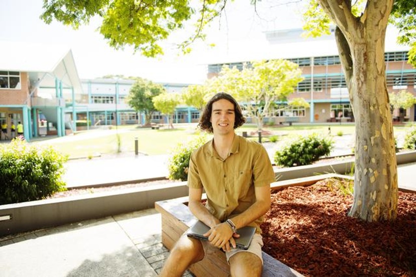 male student sitting on front of Coffs campus buildings