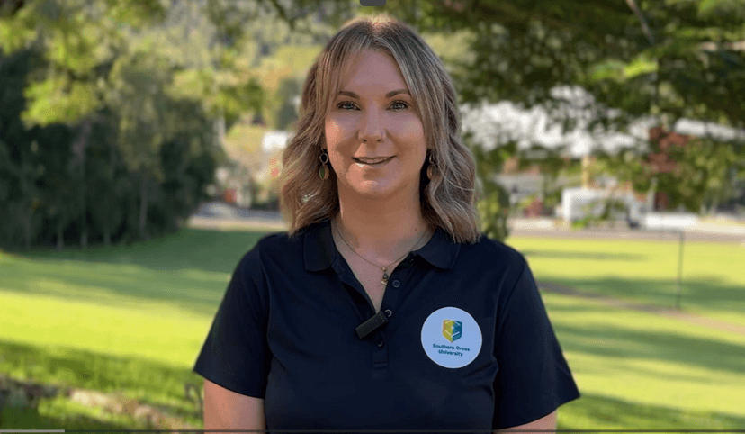Woman in SCU shirt presenting to camera with a background of green trees and plants