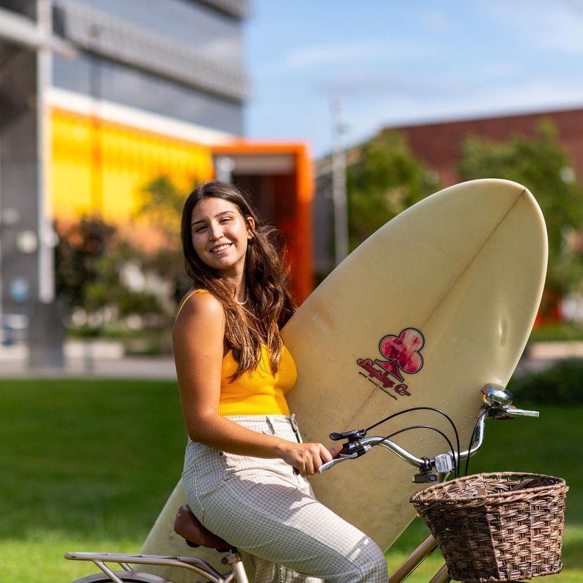 Student at gold coast campus sitting on a bike with surfboard underarm