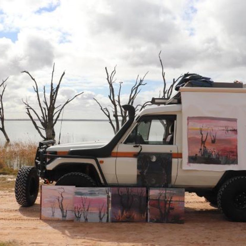 Four wheel drive vehicle with several artworks leaning on it parked beside a lake