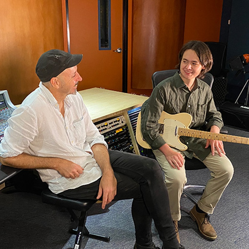 man on left with student holding guitar in music studio