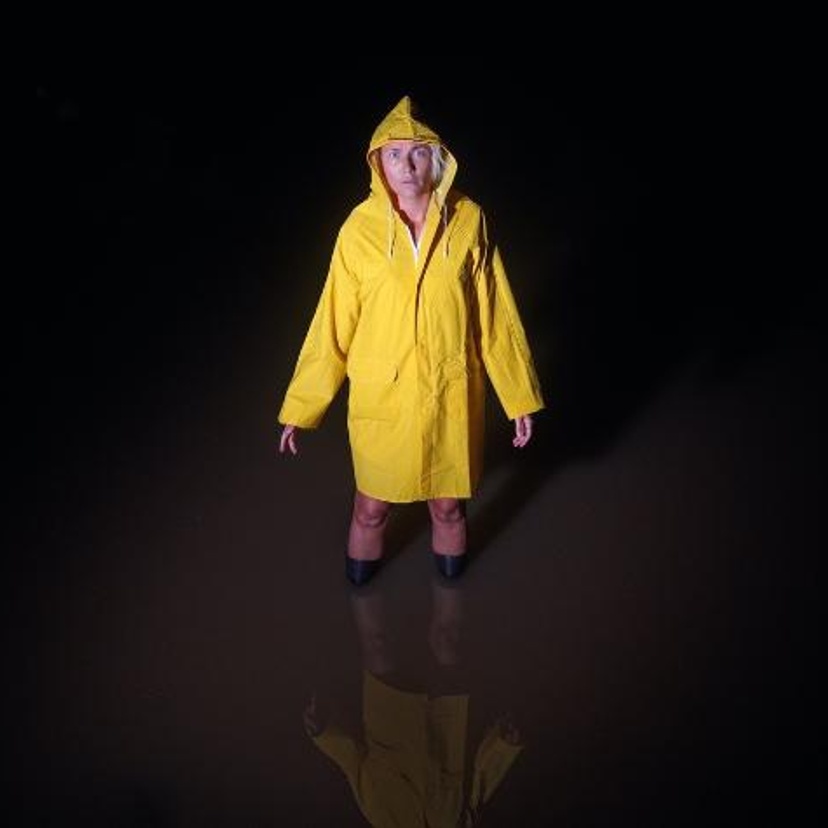 Woman in a yellow raincoast and wellington boots standing in kneehigh water