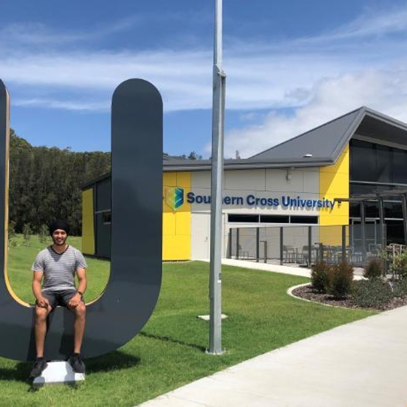 Student sitting on a large U-shaped letter outside a Southern Cross University building