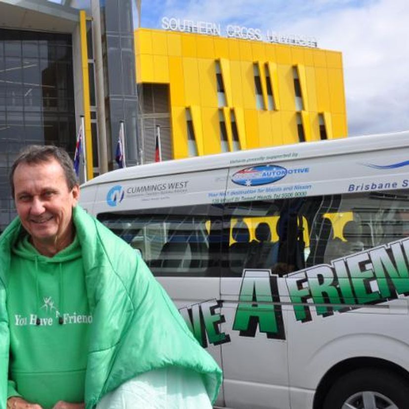 Man wrapped in a green sleeping bag standing in front of a van and a University building