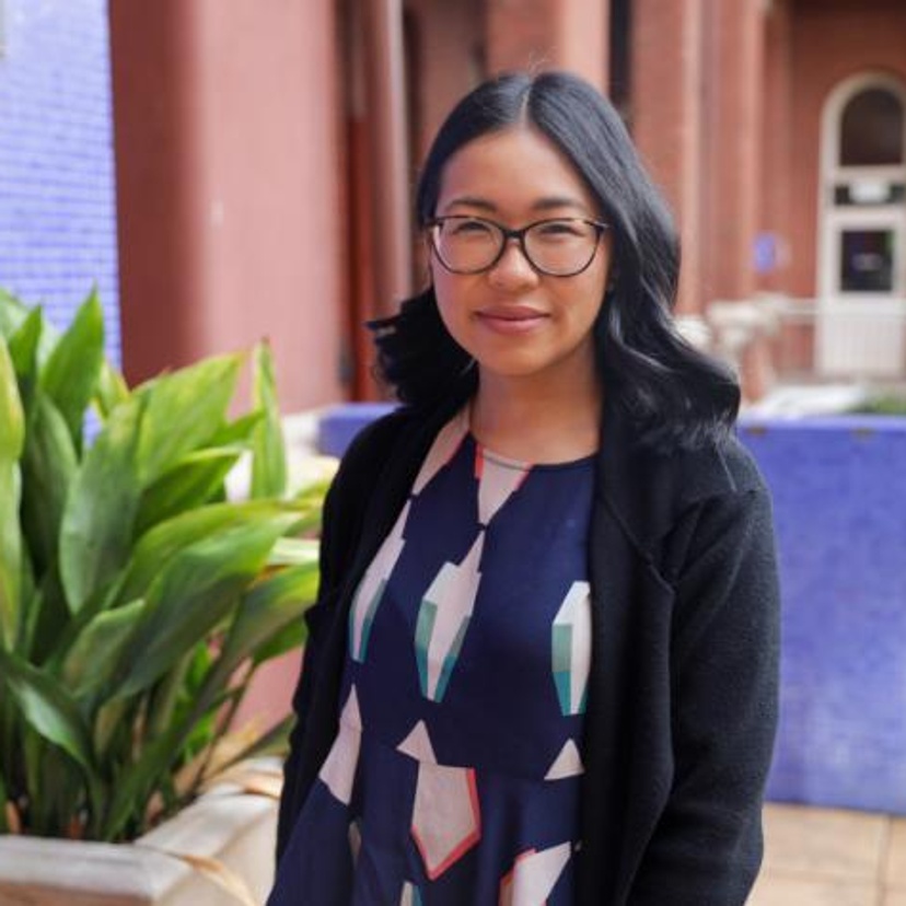 A woman with dark hair and spectacles standing in front of a building
