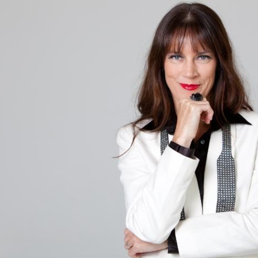 A woman with long dark hair wearing red lipstick and a white suit