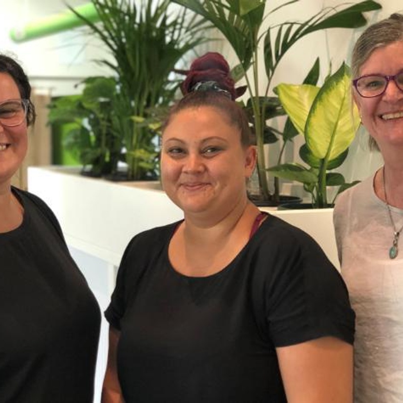 Three women in an office setting in front of pot plants