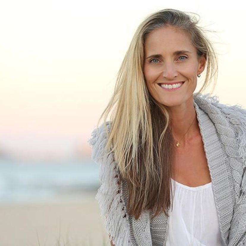A woman with long blonde hair wearing grey jumper at the beach