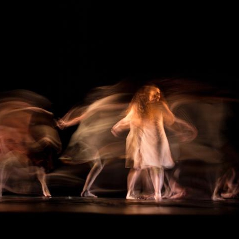 A woman with long hair and white dress moving across a stage