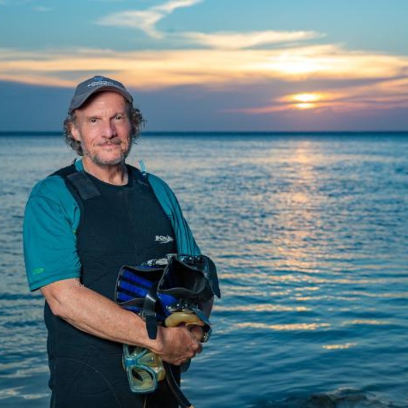 A man wearing a SCU logo hat, wetsuit and holding snorkel gear