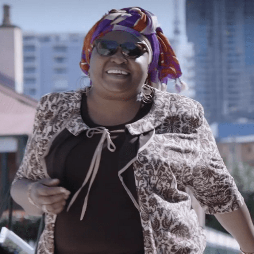 A smiling woman wearing sunglasses, handbag over arm, walking in a city