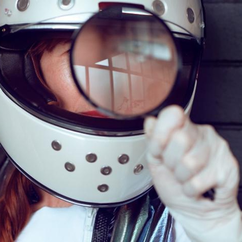 Lady in helmet looking through magnifying glass