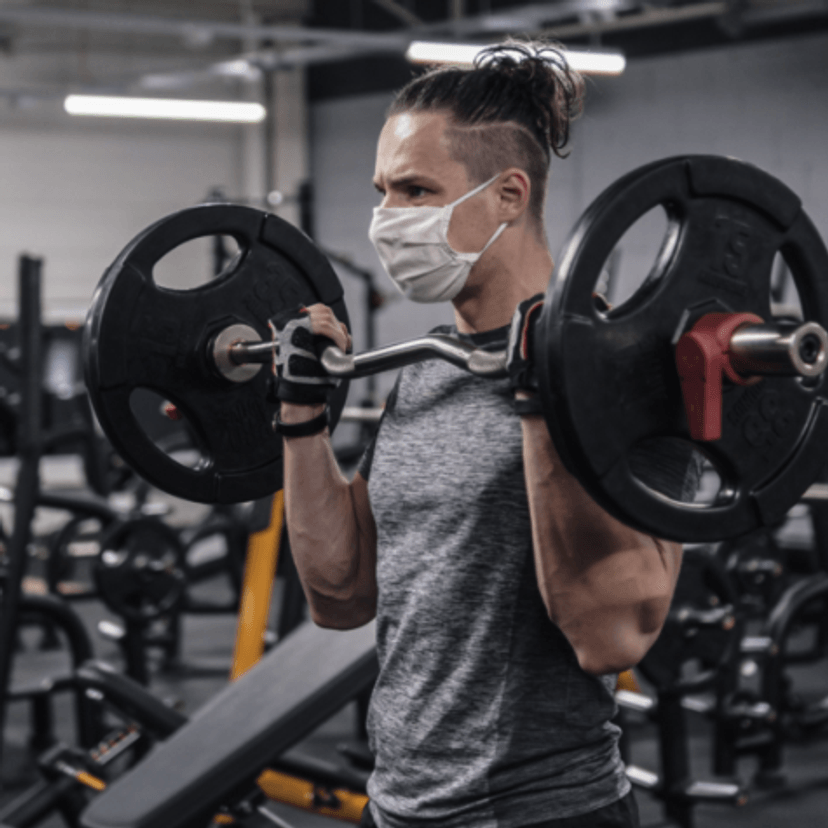 Man wearing a mask lifing weights in a gym