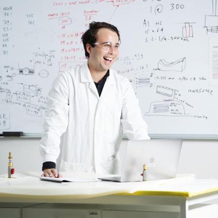 Engineering student in lab coat in front of whiteboard with mathematical calculations