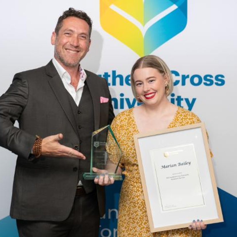 A man and a woman standing with a trophy in front of a colourful background
