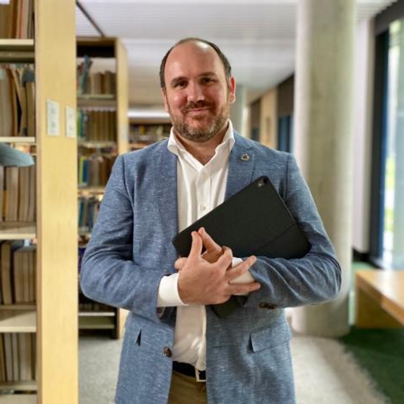 Man wearing suit holding a laptop in library