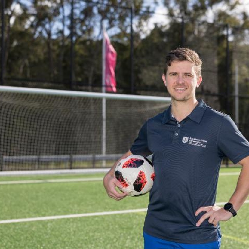 A man with a football stands in from of a soccer net