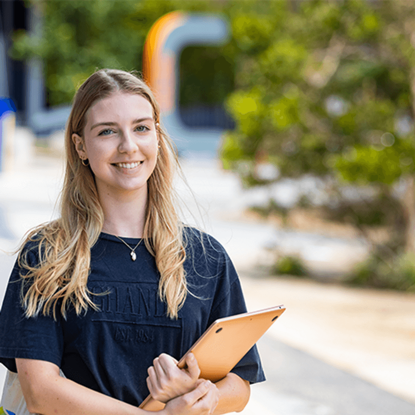 Student standing at Gold Coast campus holding laptop