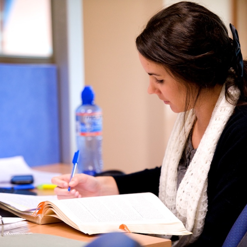 A student doing research at a desk with pen and paper