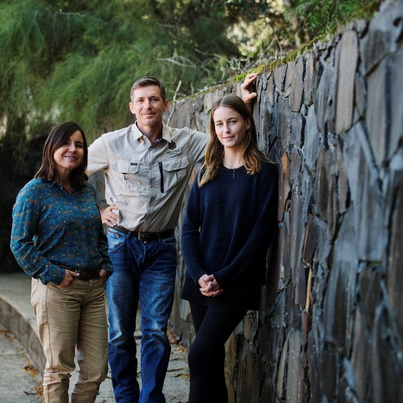 Three people standing next to a stone wall