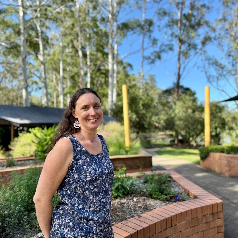 A woman standing in a garden of herbs, trees in the background