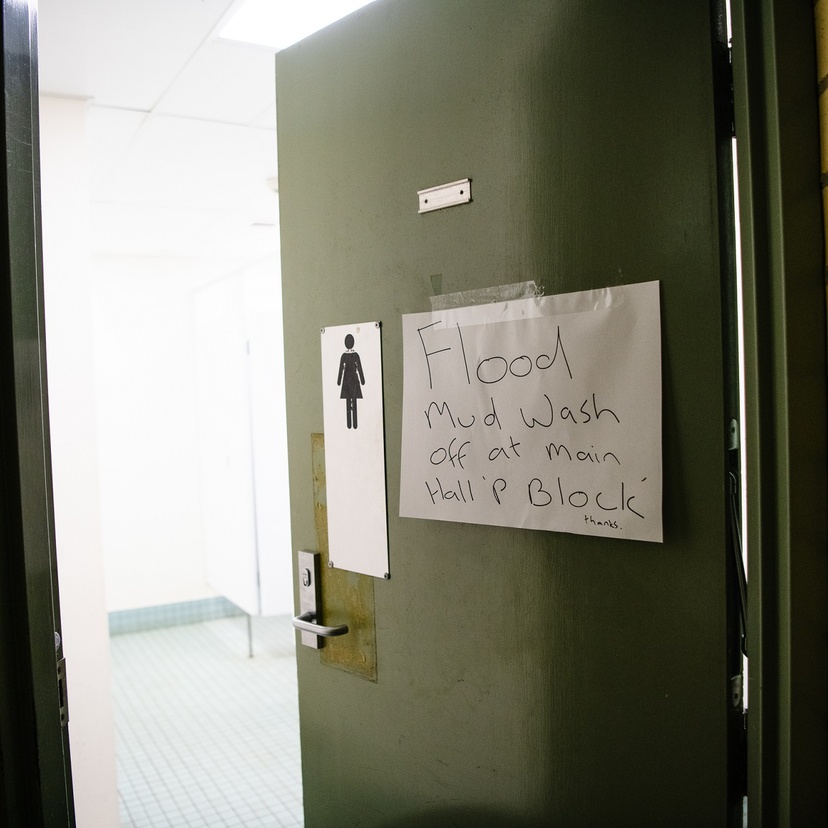 A sign on a bathroom door reads 'Wash flood mud off at Main Hall P Block'
