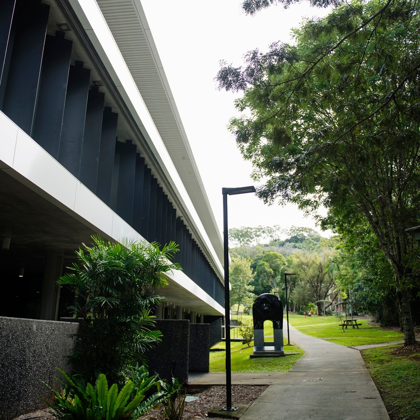 A modern campus building with a green rainforest backdrop