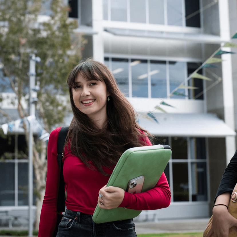 Students walking through Gold Coast campus grounds holding laptop