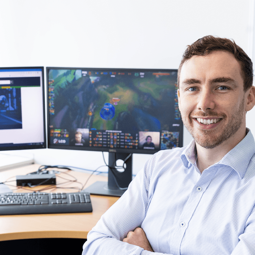 Man smiling at camera sitting at desk with video game on computer