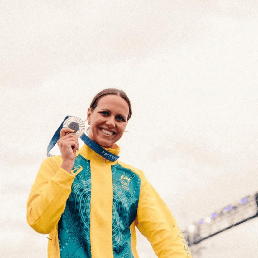 Athlete in yellow and green jacket holding silver medal with Eiffel Tower in background
