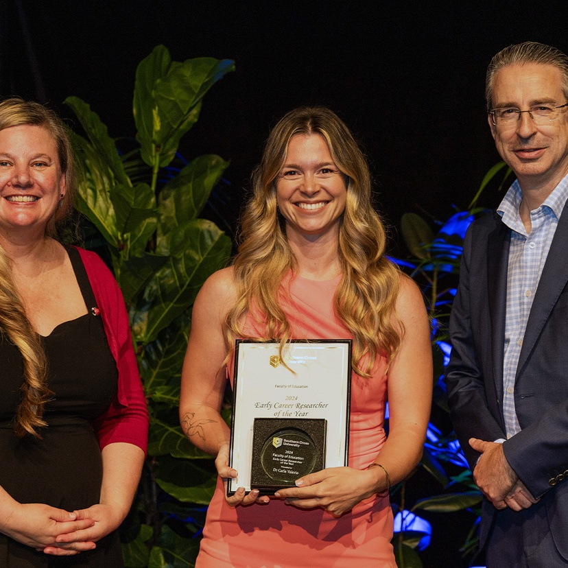 Two women and man smiling at camera. Woman in centre holding an award