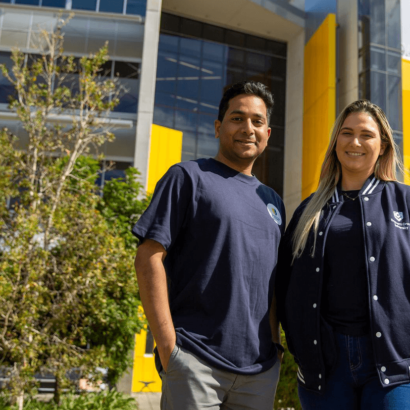 Man and woman smiling at camera in front of yellow building