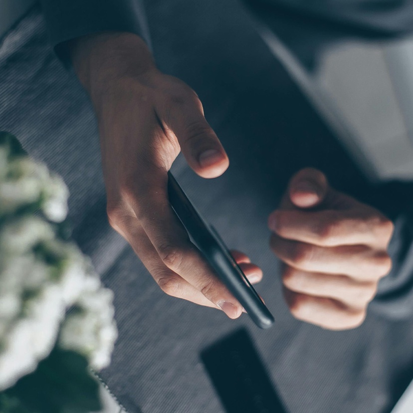 An aerial shot of two hands using a smartphone, with flowers to the side
