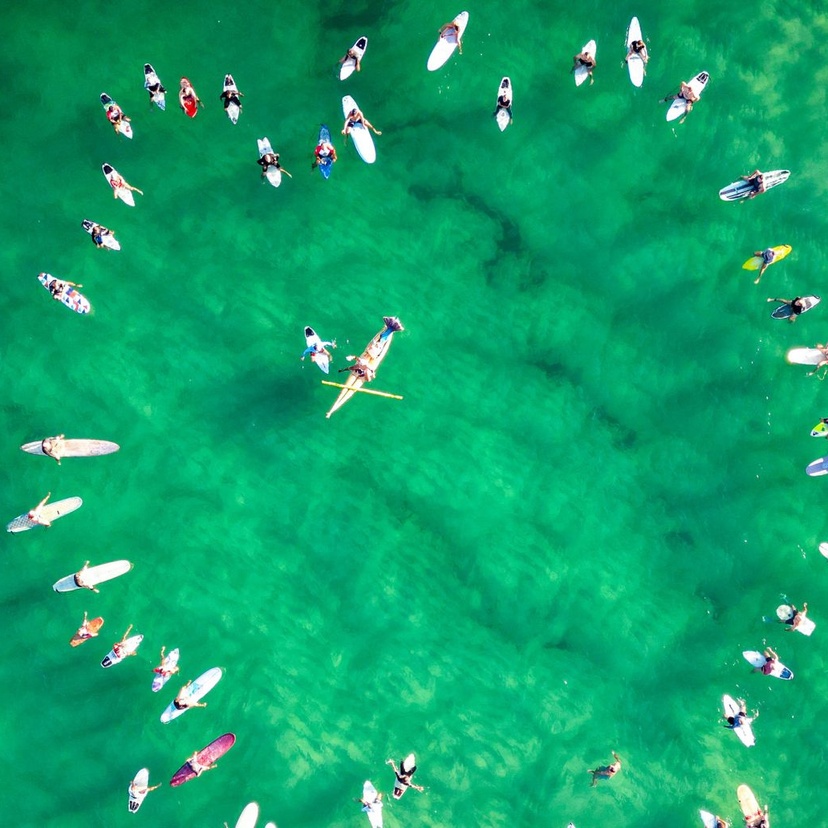 Aerial shot of surfers on surfboards forming a love heart in the ocean
