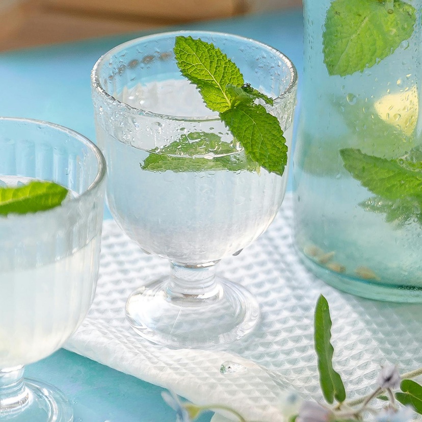 Two glasses with water and mint and a jug of water and mint on blue table