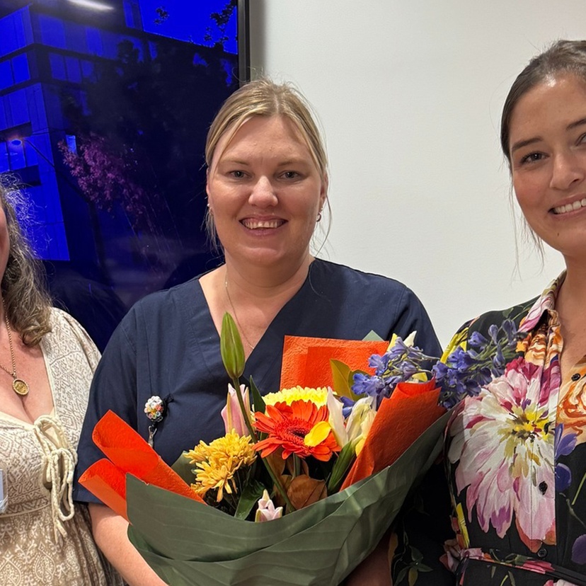 Three women smiling, the middle person holding bouquet of flowers