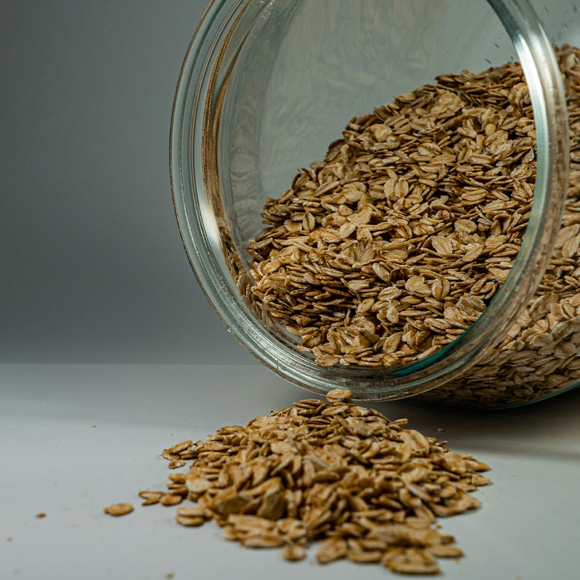 A glass jar of oats spilling onto a white counter