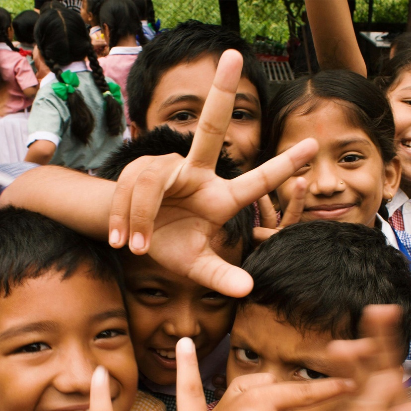 A group of young children crowding camera and holding hands up