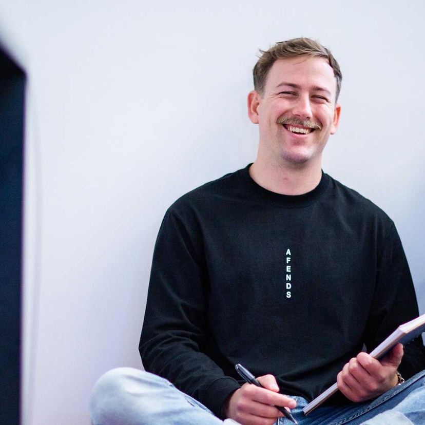 Nathan smiling sitting cross-legged with notebook and pen