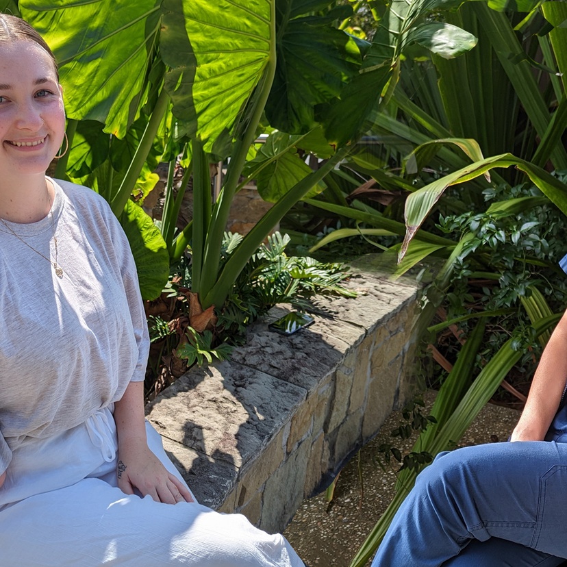 Two women seated with a green leafy background