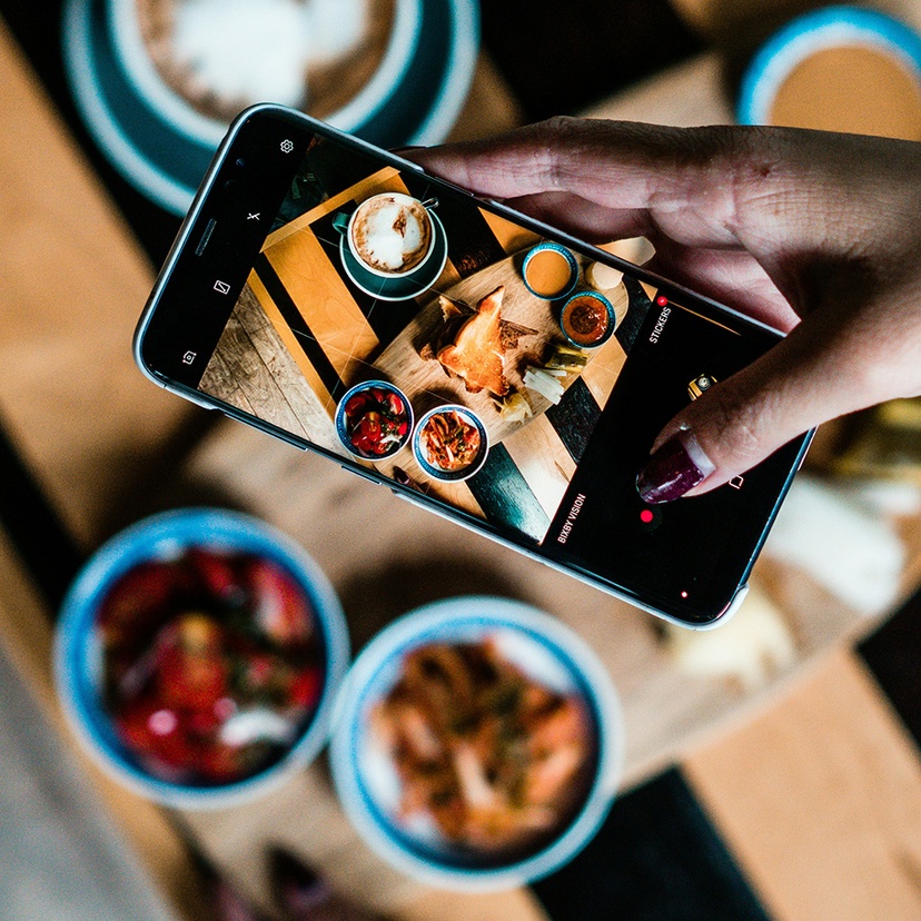 Person with a mobile phone takes a photo of the food on a table.