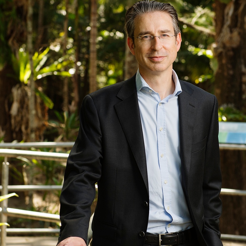 A man in a business suit and open shirt standing outside in a garden.