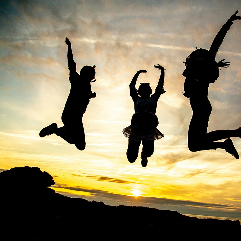 Teenagers jumping against sunset sky