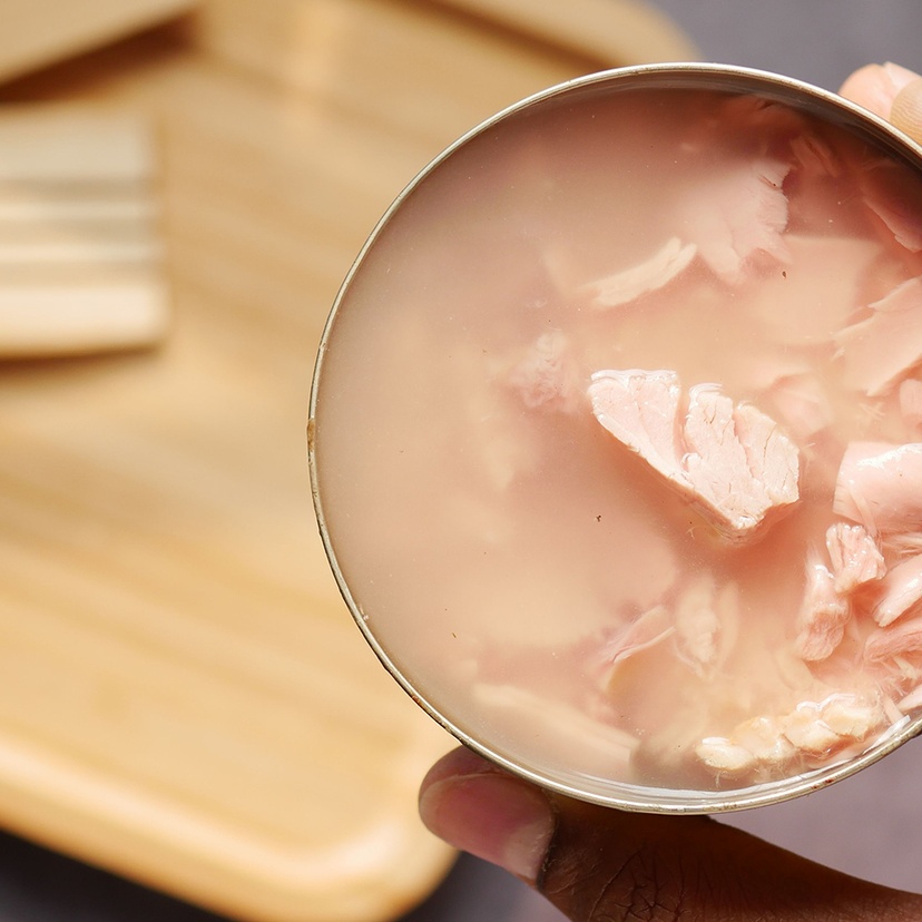 An open can of tinned tuna next to a wooden cutting board