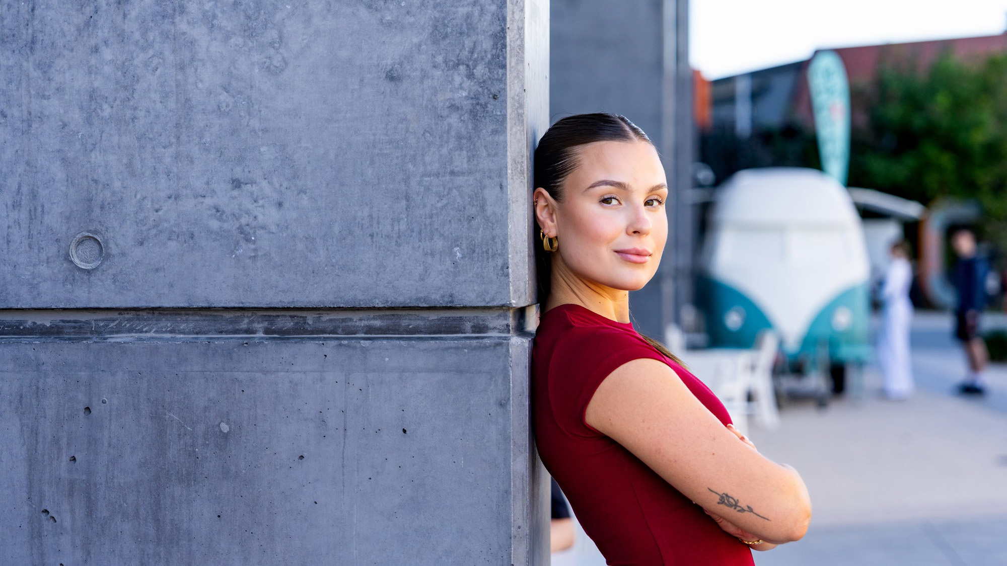 Young woman in red shirt leaning with back against cement pillar