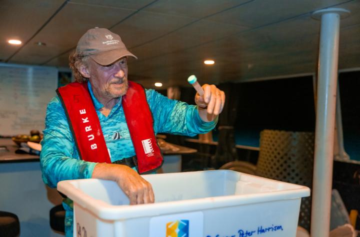 A man working on a boat at night with a testtube filled with coral spawn