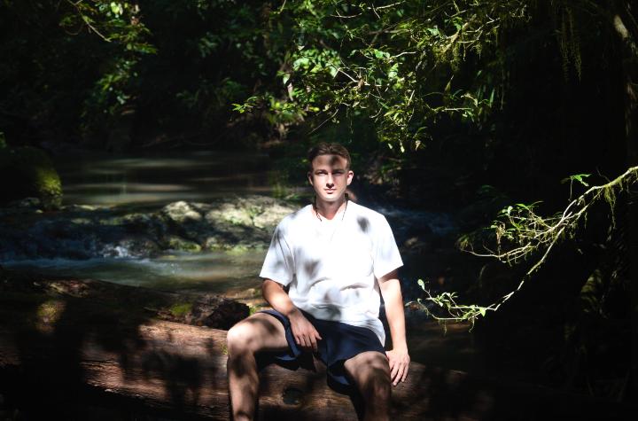 Events and News A boy sits on a tree trunk in a creek