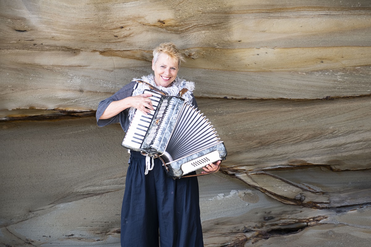 A woman playing an accordion in front of a sandstone rockface