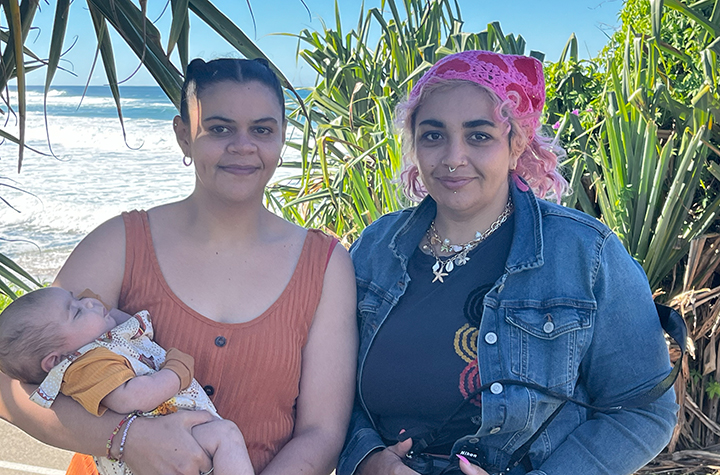 Two women outside, one holding a baby, the other with pink hair